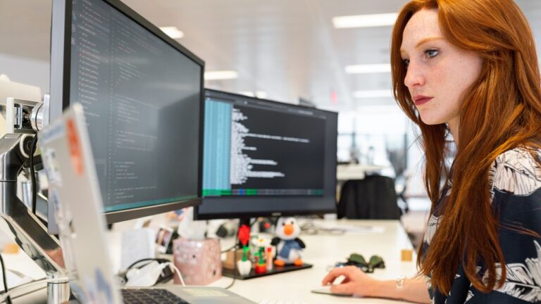 Gestructureerde data in de praktijk: vrouw werkt achter twee beeldschermen met code op kantoor